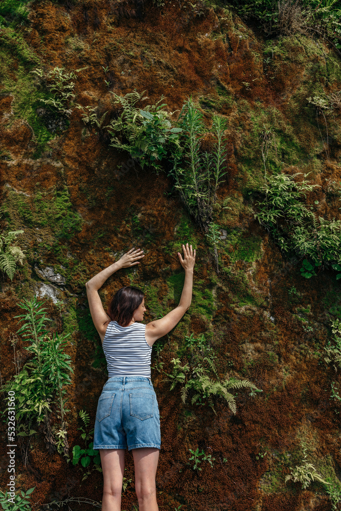 A slender girl clung to a green rock with plants and moss for cooling A slender girl clung to a green rock with plants and moss for cooling