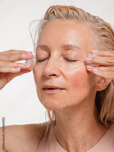 Woman with closed eyes applies the ice to face - isolated on white photo