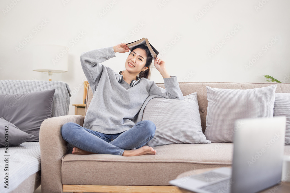 Beautiful Asian woman reading a book in her living room at home.
