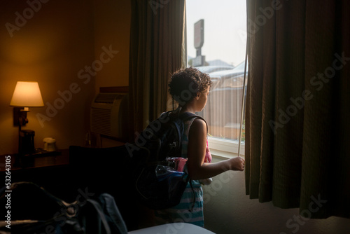Girl with backpack looks out hotel window