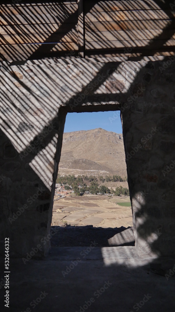 Photo prise à l'intérieur d'une petite maison en ruine et vers une porte, sur le flanc d'une haute montagne péruvienne, en plein jour