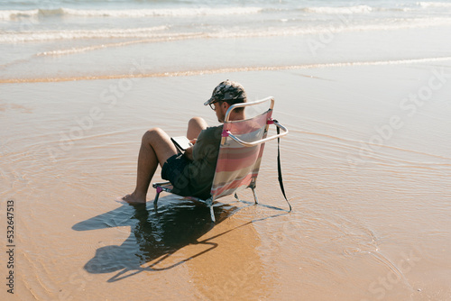 Man on folding beach chair reading at the beach