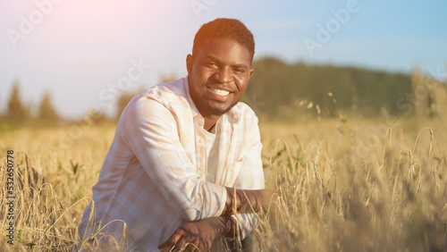 Billede på lærred African American agriculturist sits on wheat field looking with smiling expression