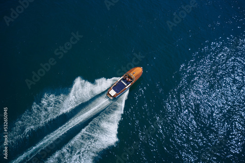 Luxurious wooden motor boat rushes through the waves of the blue Sea. Classic Italian wooden boat fast moving aerial view. Luxurious wooden boat fast movement on dark water.