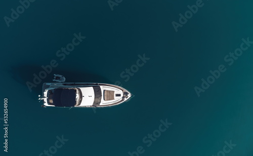 Aerial yacht on calm sea. Luxury cruise trip. View from above of white boat on deep blue water. Aerial view of rich yacht sailing sea. Summer journey on luxury ship. © panophotograph