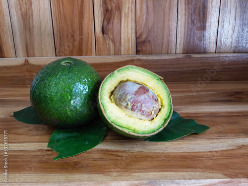 Green avocado fruit with sliced and leaves on wooden background.