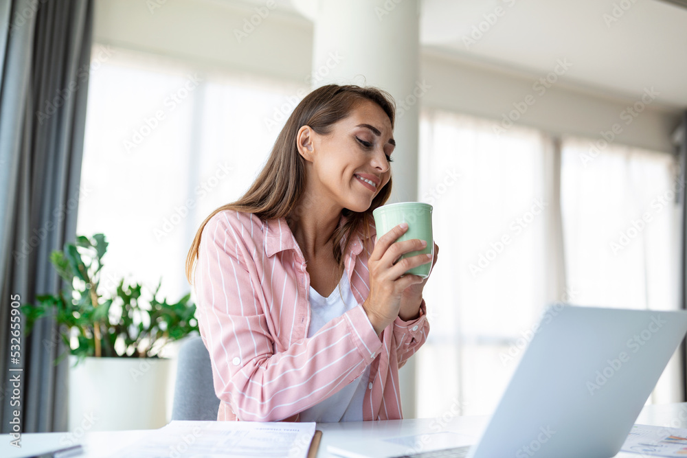 Positive young woman freelancer watching video in blog on netbook and having a coffee at comfortable office. Beautiful young business woman working on laptop.Freelancer connecting to internet Positive young woman freelancer watching video in blog on netbook and having a coffee at comfortable office. Beautiful young business woman working on laptop.Freelancer connecting to internet