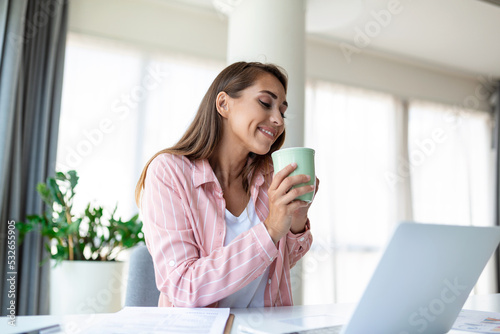 Positive young woman freelancer watching video in blog on netbook and having a coffee at comfortable office. Beautiful young business woman working on laptop.Freelancer connecting to internet