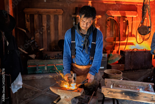 Cowboy steel farrier hoseshoe maker in the shop burn red hot steel piece in the fire blower stove fire dust and smoke fly in the air and hammer steel curve on anvil  

