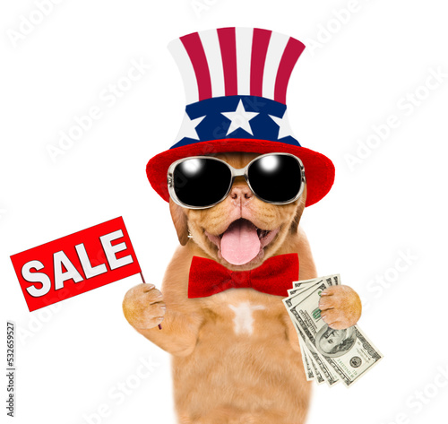 Happy Mastiff puppy wearing like Uncle Sam holds dollars USA and shows signboard with labeled "sale". isolated on white background © Ermolaev Alexandr