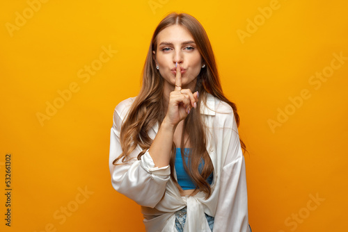 Pretty young woman holding finger on lips and showing silence sign on yellow background photo