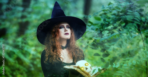 Konstfotografi Young witch with spell book and skull in green forest