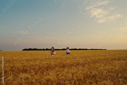 Parents holding children in arms and walking in wheat field at sunset, father hugging son. Loving family in countryside. Concept of bonding