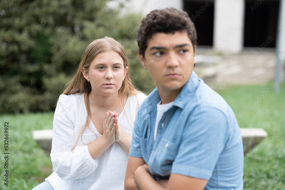 Teenager girl aking for forgiveness at angry boyfriend ignoring her. Couple relationship in adolescence concept.