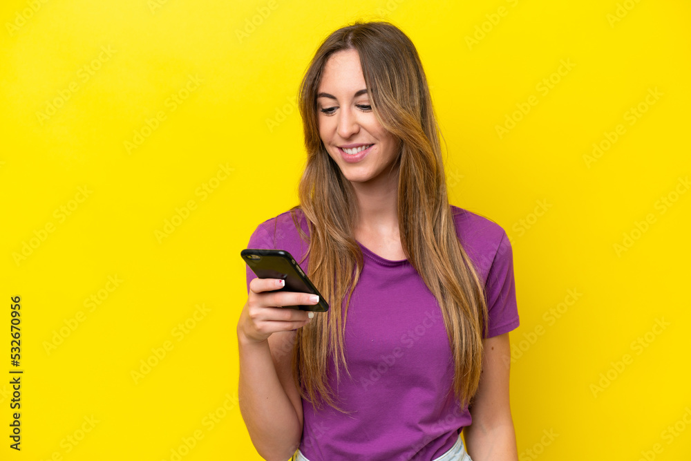 Young caucasian woman isolated on yellow background sending a message or email with the mobile Young caucasian woman isolated on yellow background sending a message or email with the mobile