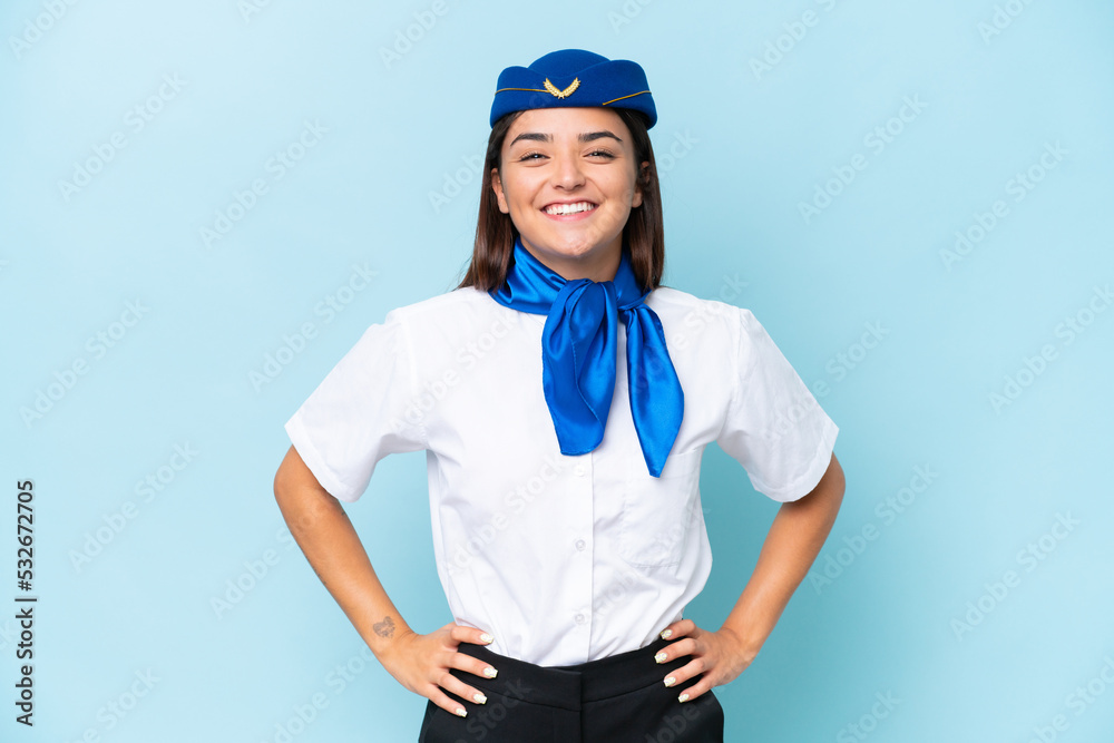 Airplane stewardess caucasian woman isolated on blue background posing with arms at hip and smiling Airplane stewardess caucasian woman isolated on blue background posing with arms at hip and smiling