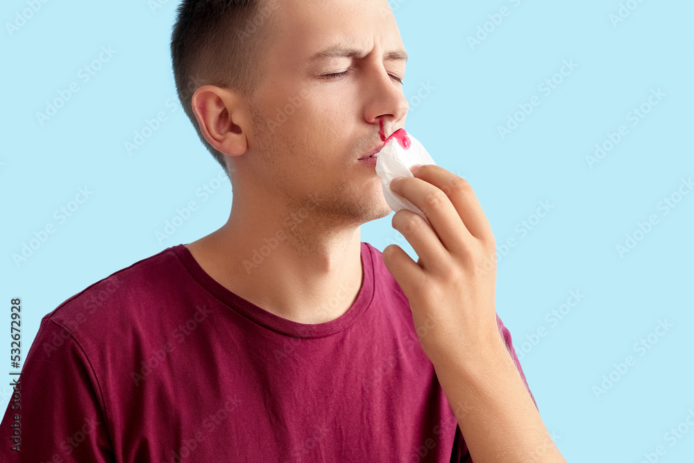 Young man wiping nosebleed with tissue on blue background Young man wiping nosebleed with tissue on blue background