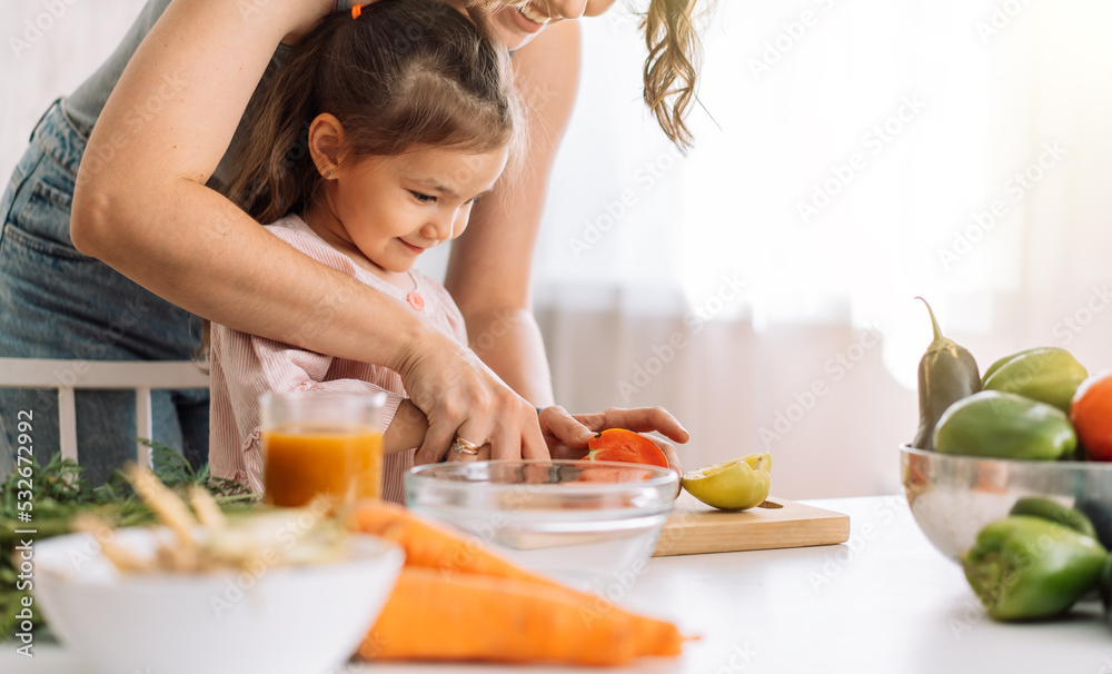 Mom and daughter cook food together slicing tomato.