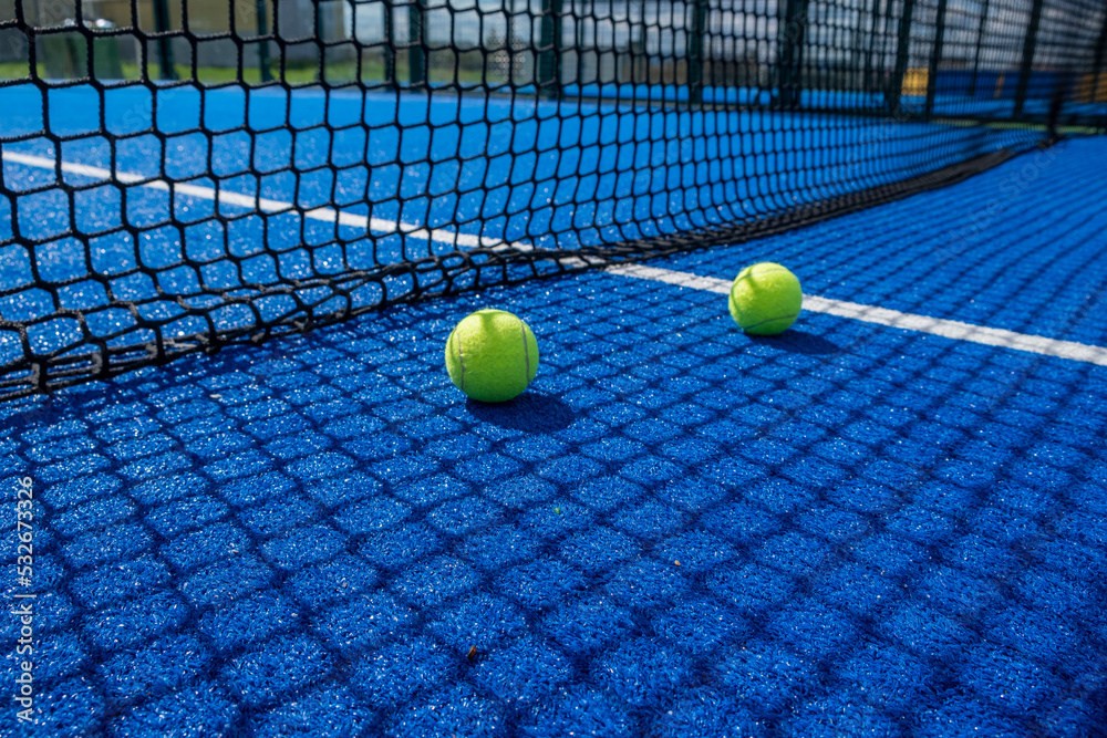 two balls near the net of a blue paddle tennis court