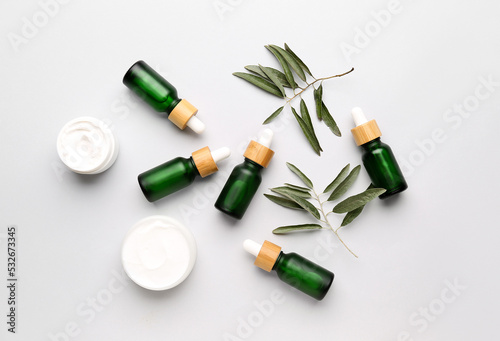 Bottles of essential olive oil and jars with cream on white background