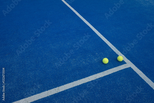 two balls next to the side of a blue paddle tennis court, racket sports © Vic