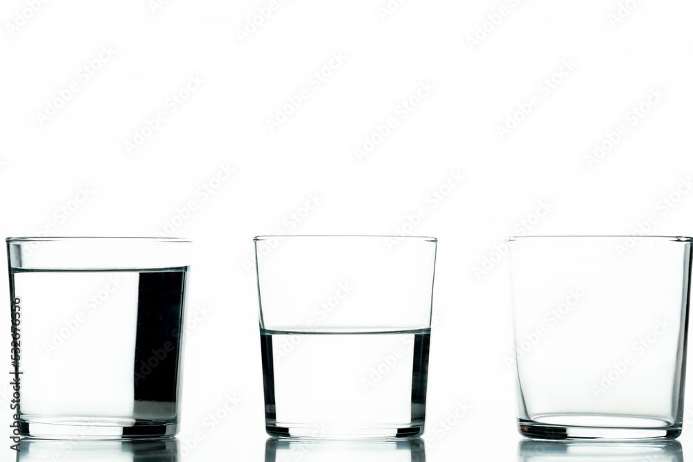 Three crystal glasses, one full of liquid, one half-full and one empty - concept of quantity and capacity Three crystal glasses, one full of liquid, one half-full and one empty - concept of quantity and capacity