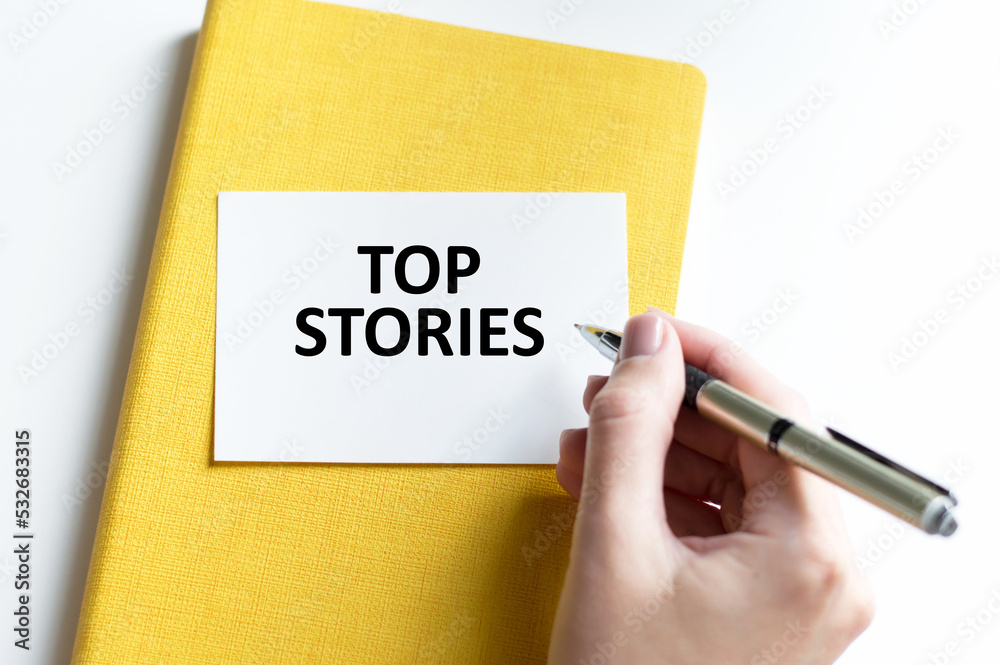Top stories text card on a yellow notebook next to a person's hand on a light background Top stories text card on a yellow notebook next to a person's hand on a light background