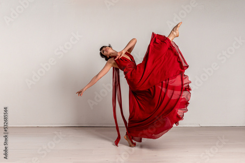 Dancer in a red flying dress. Woman ballerina dancing on a white studio background