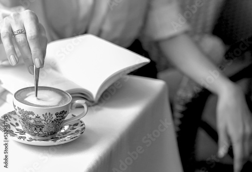 A cup of capicino with a blue pattern on a table in a cafe. Female figure sitting in a cafe. © Alina