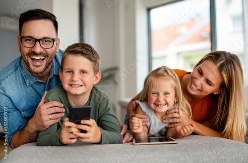 Happy young family having fun time at home. Parents with children using digital device.