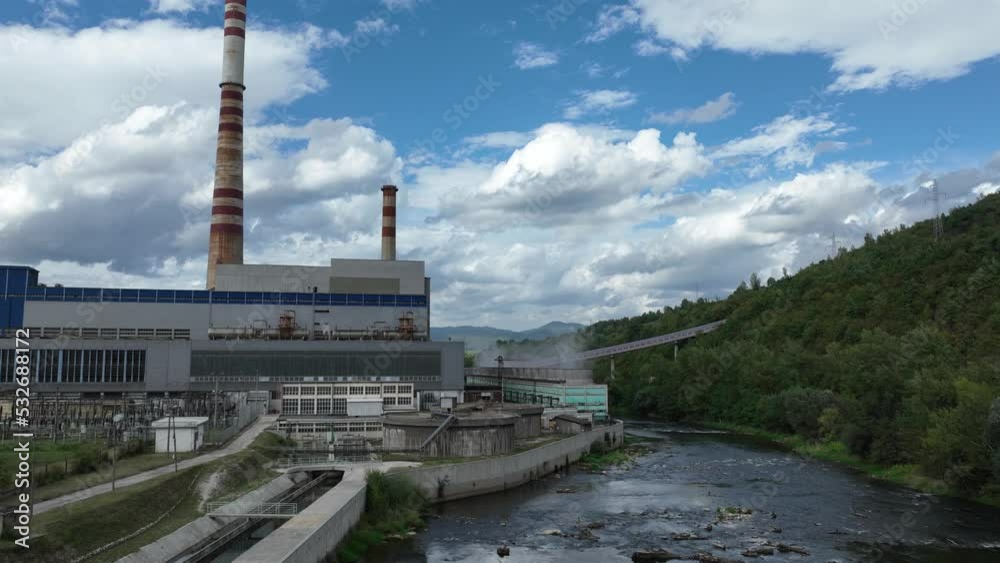 Aerial 4k time lapse or hyperlapse of coal power plant with two high cooling towers next to blue river. Smoke coming out of chimney and steam from power generation turbines. 