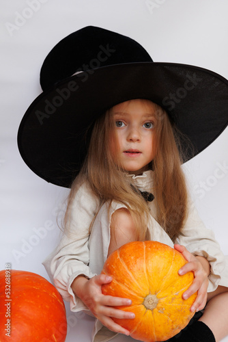 Halloween portrait of a little girl in a witch magic hat. Little child with pumpkins. White background.  photo