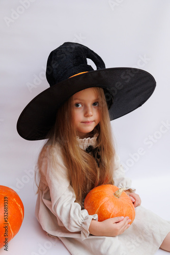 Halloween portrait of a little girl in a witch magic hat. Little child with pumpkins. White background.  photo