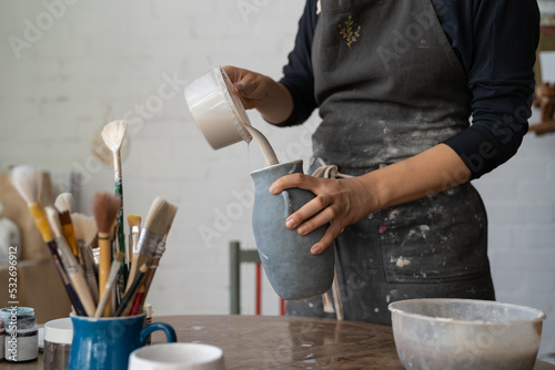 Φωτογραφία Craftsmaster wearing dirty apron pours liquid from plastic bowl into grey vase