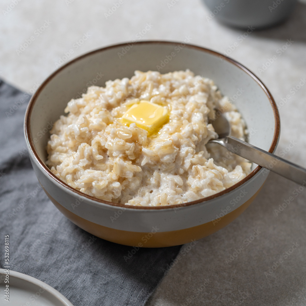 Unusual healthy delicious rice pudding made from brown rice and plant based milk served with butter and honey in grey bowl Unusual healthy delicious rice pudding made from brown rice and plant based milk served with butter and honey in grey bowl