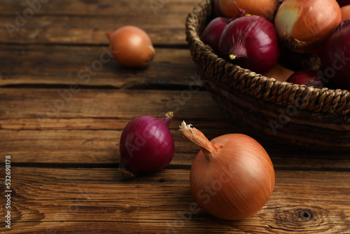 Onion bulbs and basket on wooden table