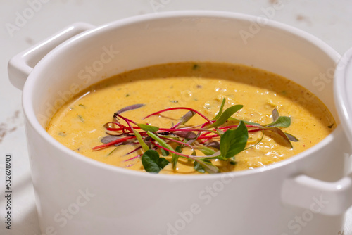 Pumpkin cream soup served with herbs in ceramic pot with lid