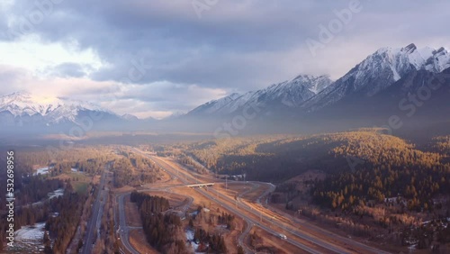 Canmore Alberta mountain range Canadian rockies surrounding highway and overpass aerial sunrise drone shot pan away. photo