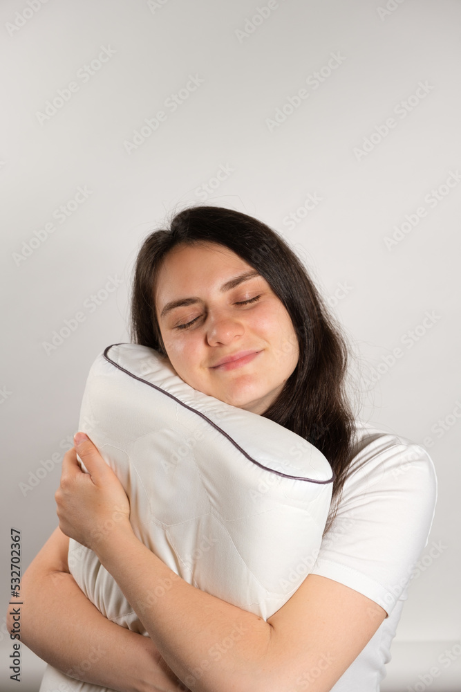 A woman hugs an orthopedic pillow made of memory foam on a white background. Choosing pillows for healthy sleep. A woman hugs an orthopedic pillow made of memory foam on a white background. Choosing pillows for healthy sleep.