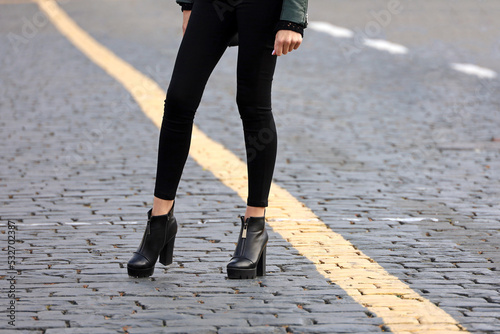 Female legs in tight black jeans and boots on high heels. Slim girl standing on a street, fashion in autumn city