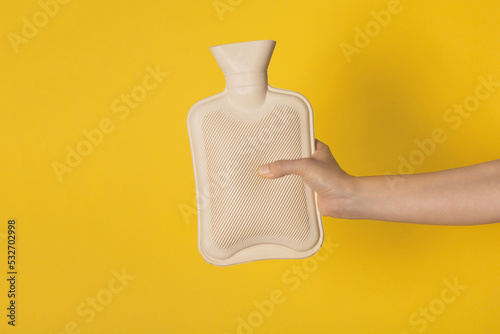 Hot water heating pad is winter essentials.  Power outages and difficulties with heating. Saving electricity. Woman holding heating pad on yellow background. photo