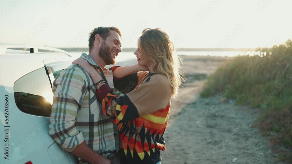 Smiling blond couple talking and hugging near car outdoors Smiling blond couple talking and hugging near car outdoors