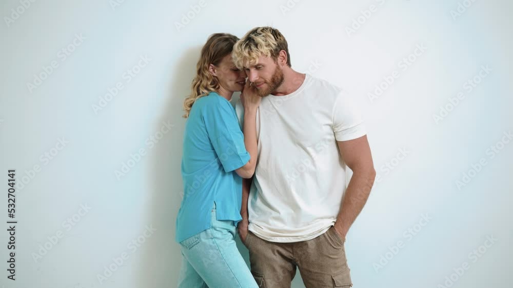 Positive blond young woman says the secret in her boyfriends ear in the white studio Positive blond young woman says the secret in her boyfriends ear in the white studio