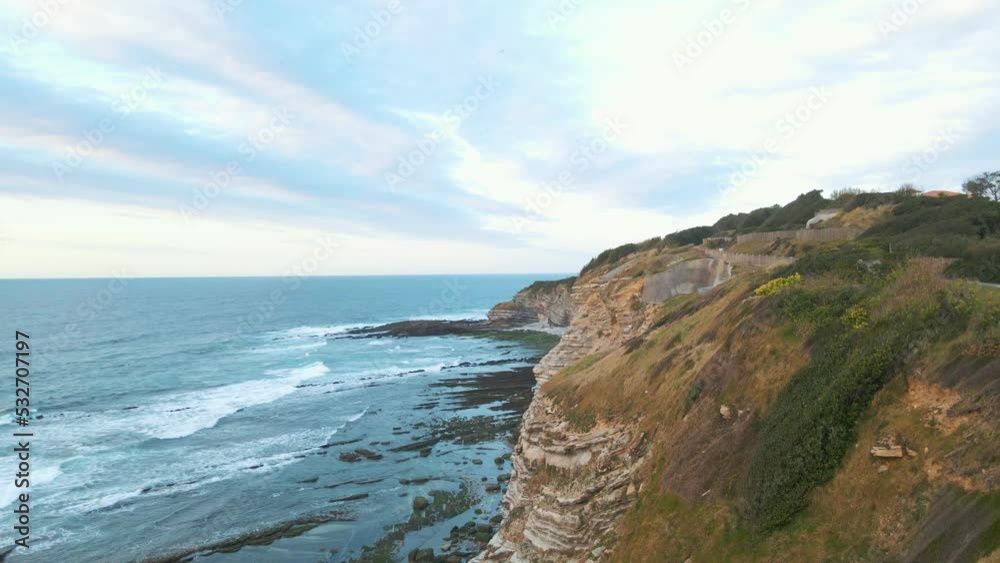Flying Over Rocky Coastline alongside Cliffside at Saint Jean de Luz in Basque Country with Blue North Atlantic Ocean Water Towards the Sun During Sunset. Flying Over Rocky Coastline alongside Cliffside at Saint Jean de Luz in Basque Country with Blue North Atlantic Ocean Water Towards the Sun During Sunset.