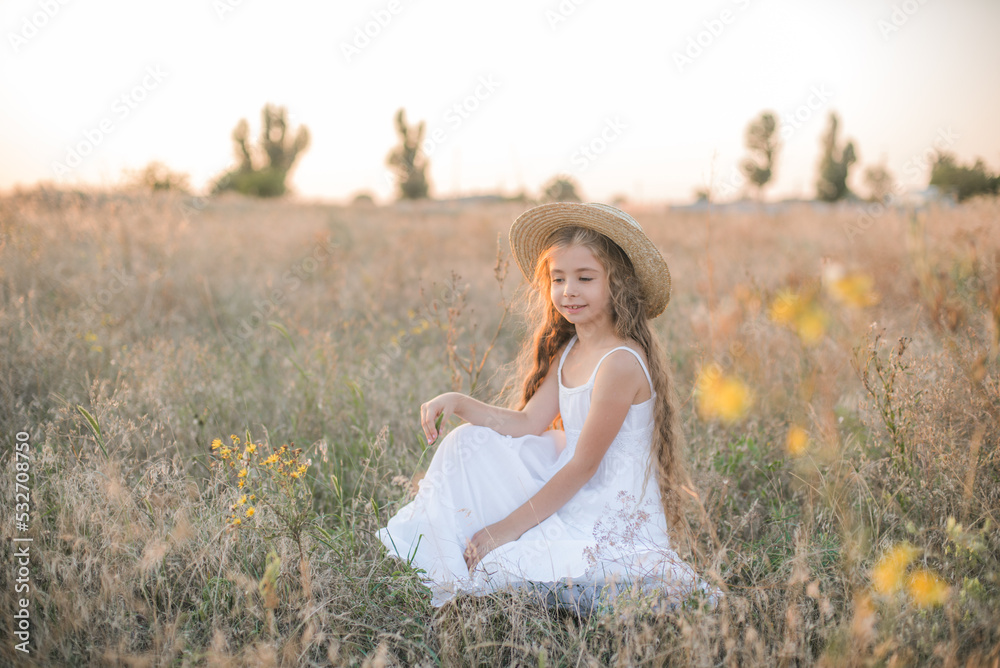 Cute little girl with blond long hair in a summer field at sunset with a white dress with a straw hat Cute little girl with blond long hair in a summer field at sunset with a white dress with a straw hat