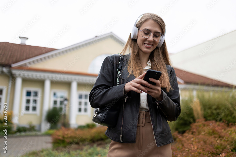 young woman goes to work listening to music in headphones via mobile phone