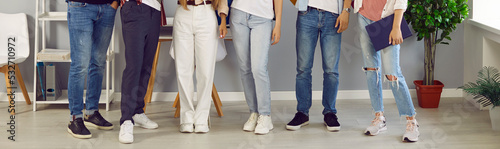 Slika na platnu Group of young people in blue jeans, white trousers and sneakers standing in row in office or in classroom