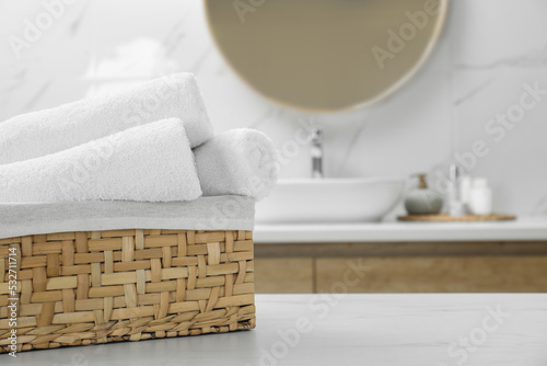 Wicker basket with rolled bath towels on white table in bathroom, space for text