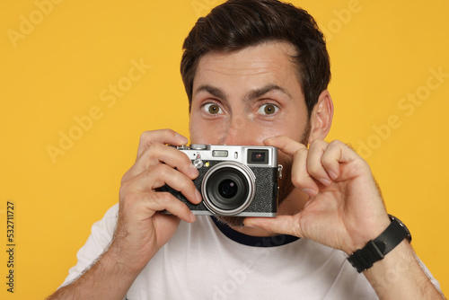 Man with camera taking photo on yellow background. Interesting hobby