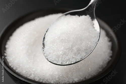 Spoon with granulated sugar over bowl, closeup